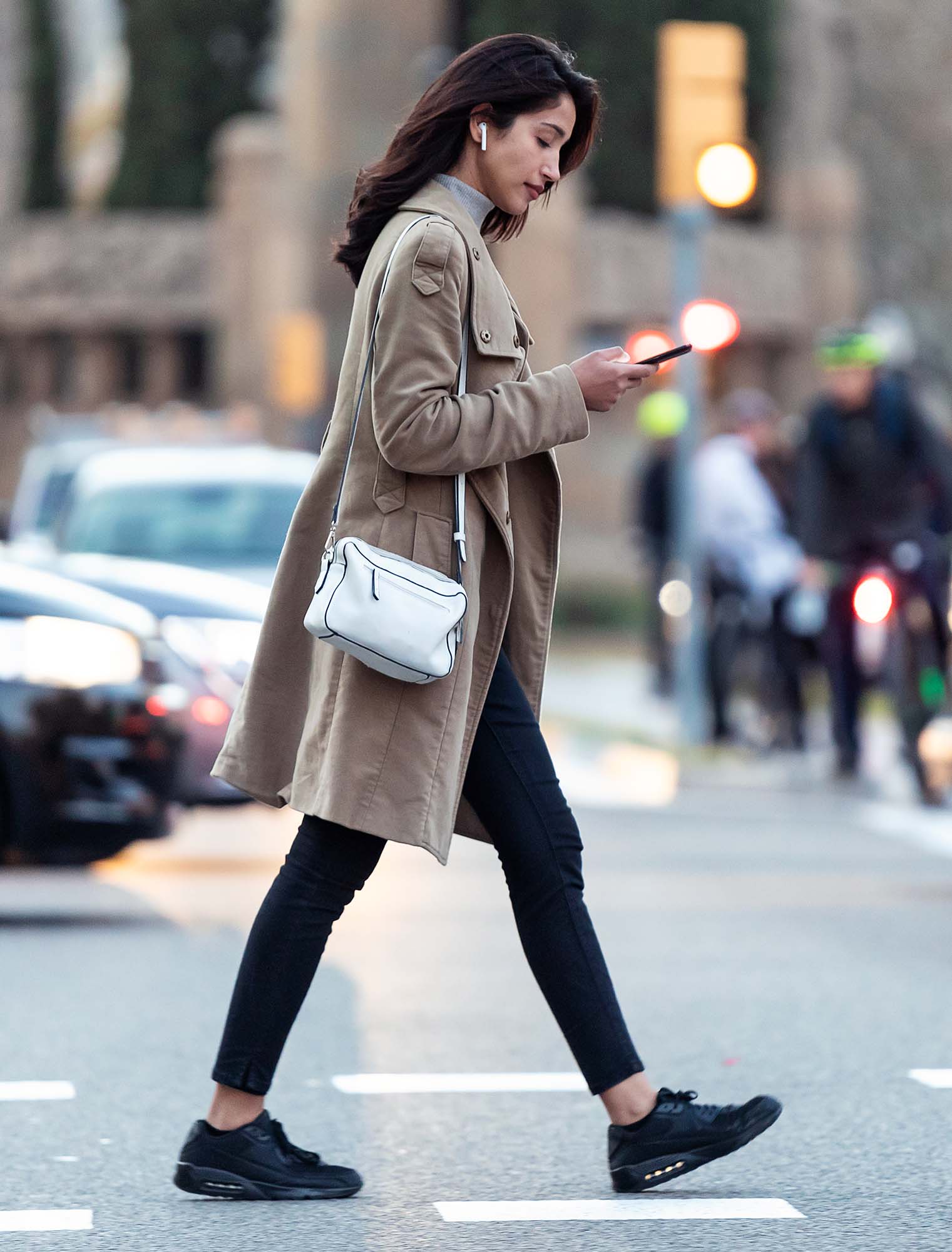 Pretty young woman crossing the street while listen to music with the wireless earphones.