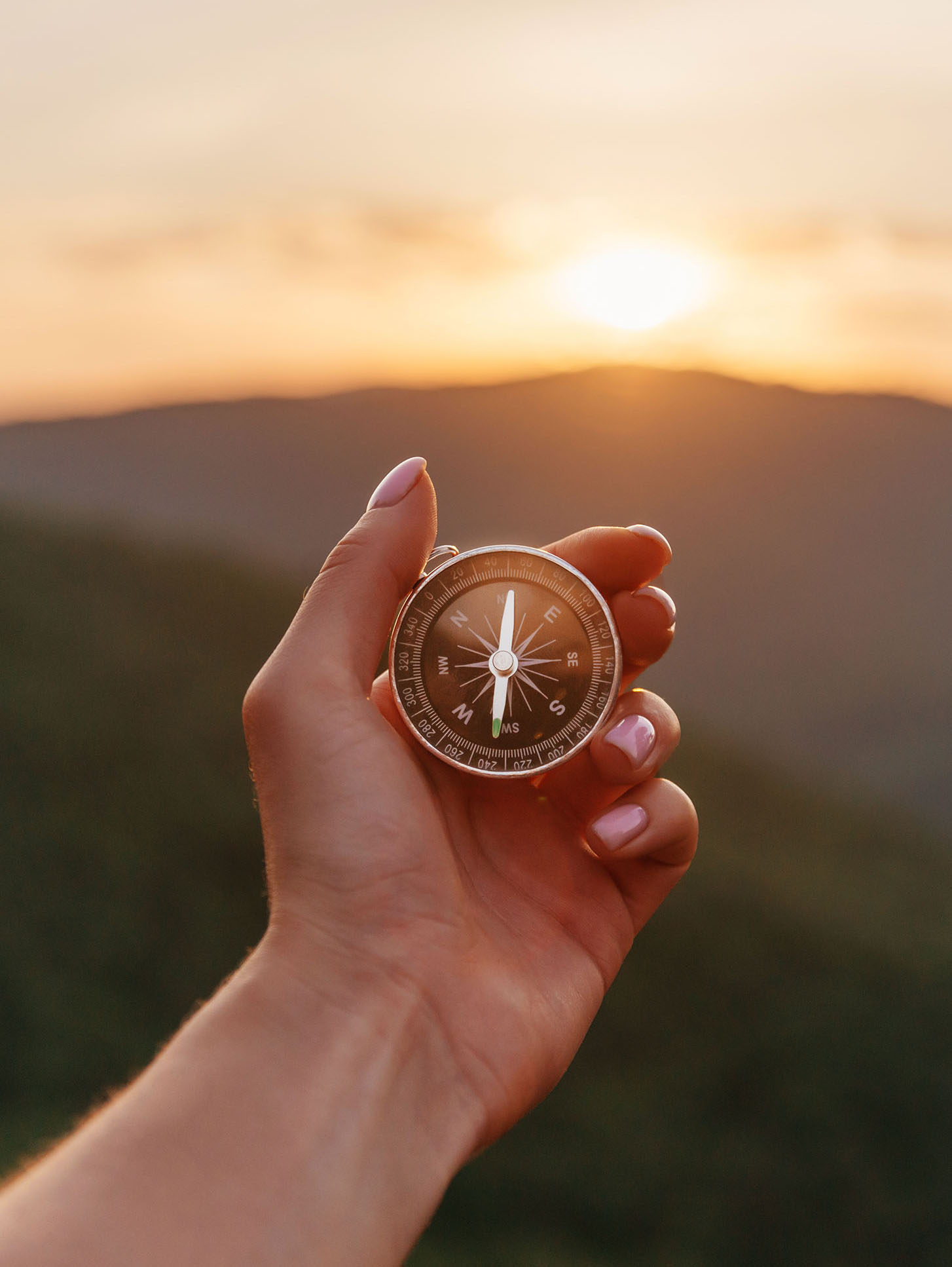 Female hand with compass in summer mountains at sunrise, pov.